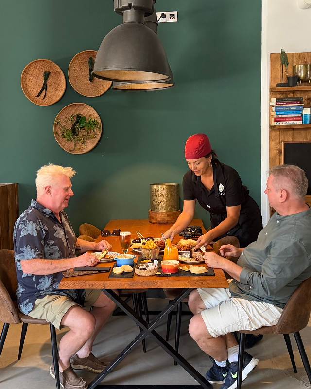 Two guests at a table with a spread of local dishes, served by the cook