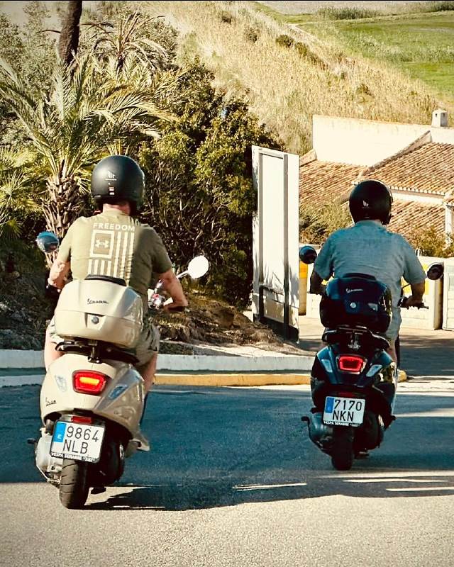 Two guests riding side by side on a beige and a dark blue Vespa